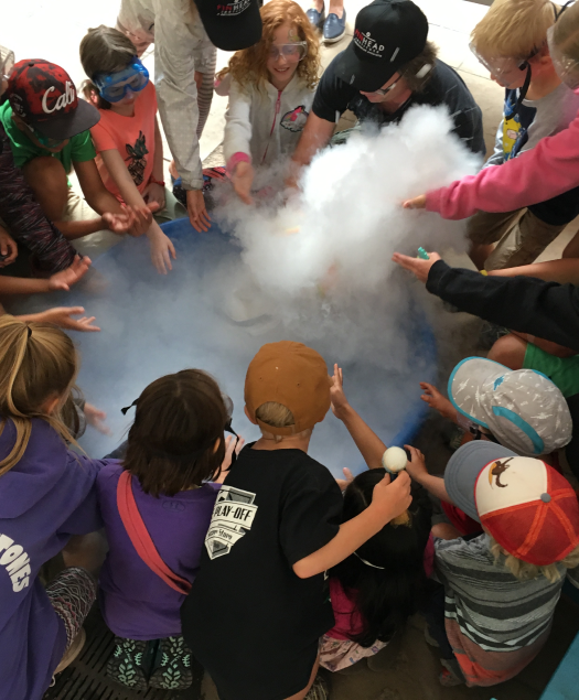 A group of young people stand around a museum activity with dry ice smoke blowing around them