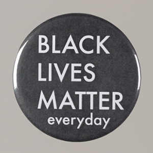 A black pinback button. It reads [BLACK/LIVES/MATTER/everyday] in white. There are several small scratches on the pin. The back is metal and does not have anything on it other than a pin at the top.