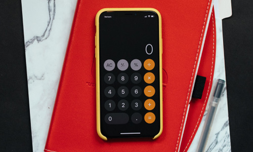 A cell phone with the calculator app open rests on a red notebook and a grey tabbed folder.