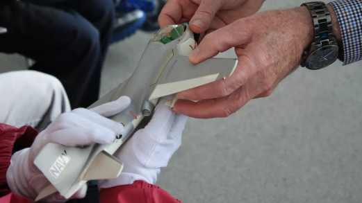 Two hands, one wearing white gloves, hold a model airplane